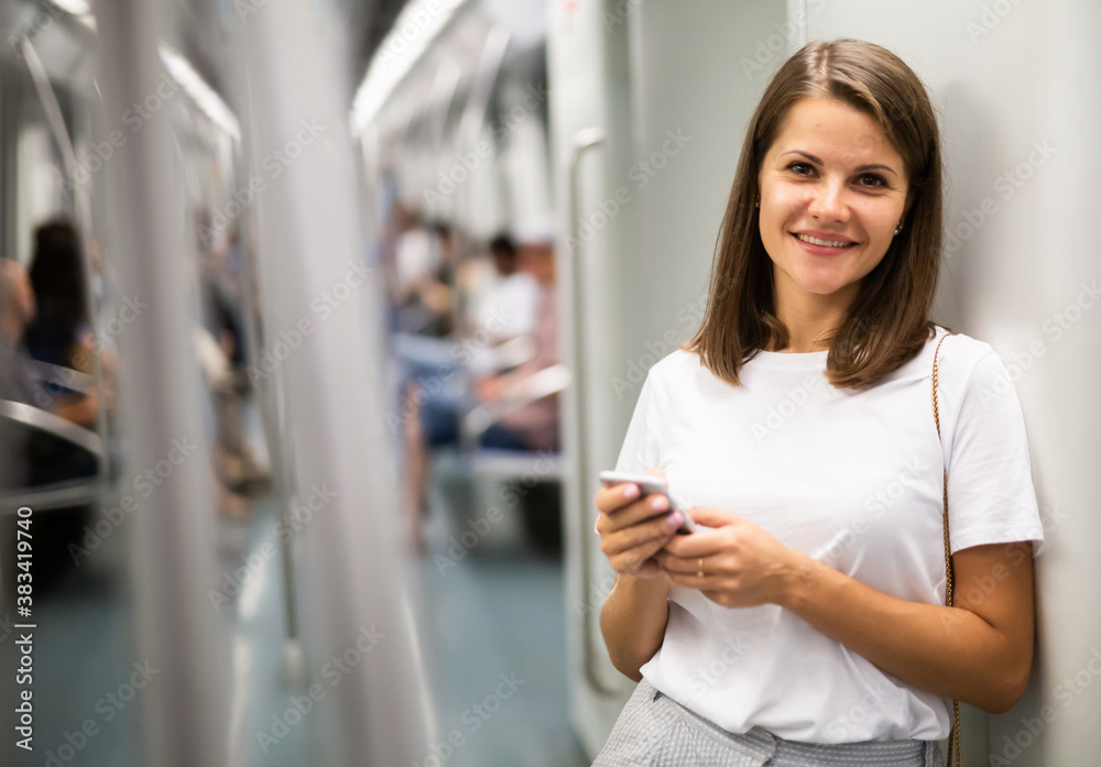 Portrait of stylish young woman holding smartphone in subway car