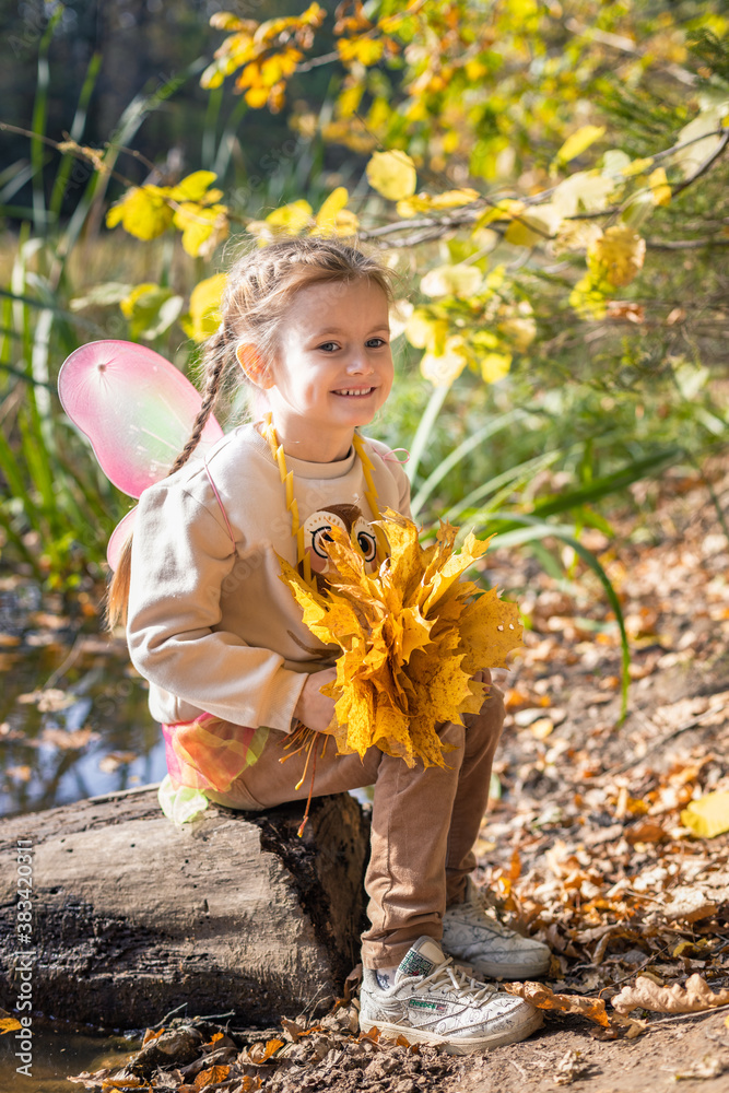 Happy little young girl with a bouquet of yellow and orange leaves resting and walking in nature in the autumn forest near the lake in Moscow region of Russia with yellow and orange autumn leaves