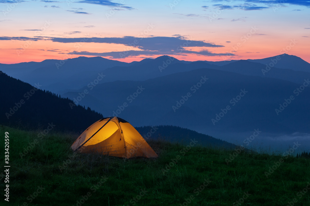 Orange tourist tent illuminated from inside on mountain
