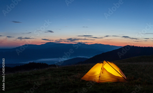 Orange luminous tent on the mountain in evening or early morning © alexlukin