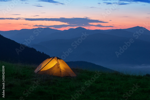 Orange tourist tent illuminated from inside on mountain