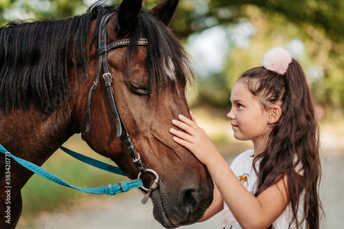 Friendship of a child with a horse. A little girl is affectionately stroking her horse. Walking girls with a horse in the park in autumn. © sergo321
