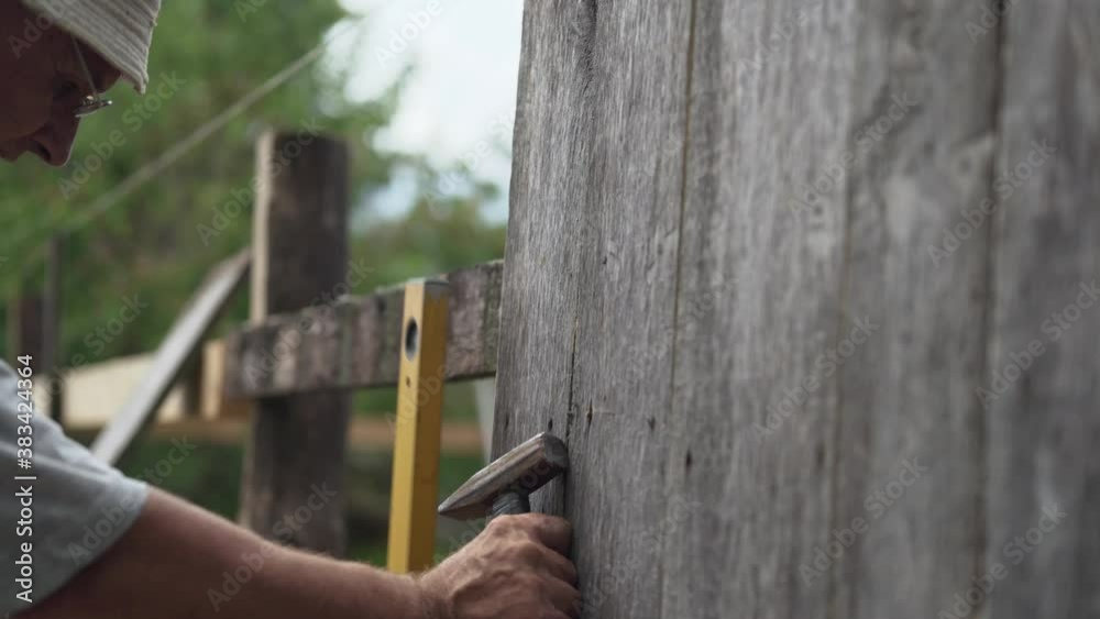 A man nails a new plank to a wooden fence. A man nails a new plank to a wooden fence.