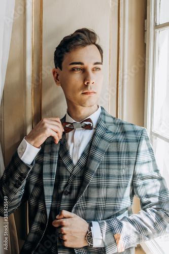 Stylish groom in an exclusive jacket posing by the window