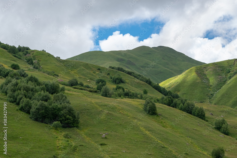 Panoramic view of green hills and green trees on blue sky background in rural Svaneti, Georgia.