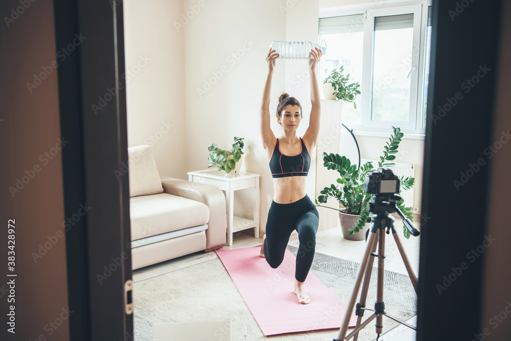 Young brunette woman with a water bottle is exercising at home wearing sportswear in front of camera Young brunette woman with a water bottle is exercising at home wearing sportswear in front of camera