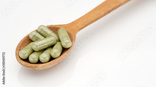 superfoods capsule moringa or spirulina in wooden spoon on white background
