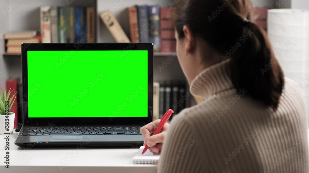 Woman is sitting at table and looking at laptop green screen, she takes notes in notebook and talking on internet online video connection. Chroma key computer screen woman talking on video call Woman is sitting at table and looking at laptop green screen, she takes notes in notebook and talking on internet online video connection. Chroma key computer screen woman talking on video call