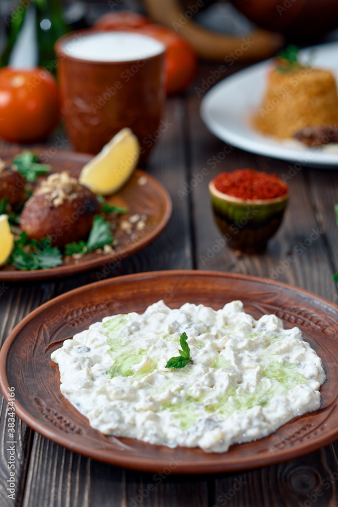 Ali nazik meze, a traditional Turkish dish of yoghurt and eggplant puree topped with a mint leaf. Side dish for kebab in a clay plate on a wooden background. Close-up, table setting. Ali nazik meze, a traditional Turkish dish of yoghurt and eggplant puree topped with a mint leaf. Side dish for kebab in a clay plate on a wooden background. Close-up, table setting.