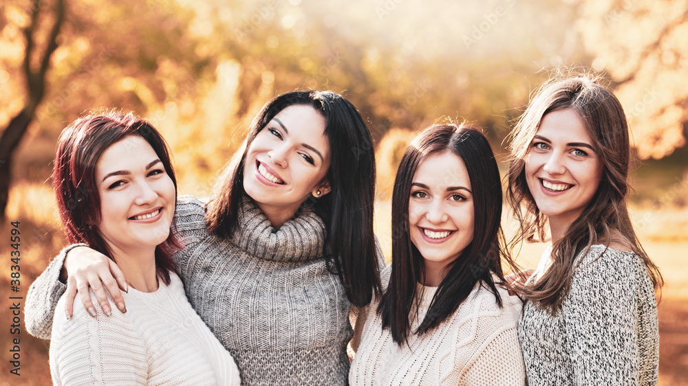 Fototapeta premium Portrait of four smiling best girlfriends posing in autumn forest