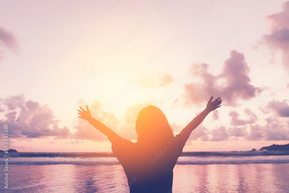 Happy woman raise hand up at tropical beach with sunset sky background. Travel vacation and freedom feel good concept.