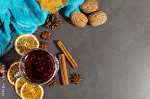 Cup of mulled wine with spices, a scarf, dry leaves and oranges on a stone table. Autumn mood, a method to keep warm in the cold, copy space.