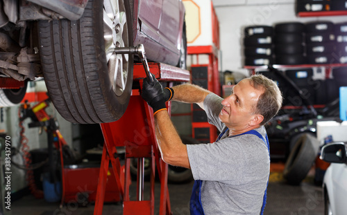 Фотография portrait of adult mechanic technician installing car wheel after repair of balan