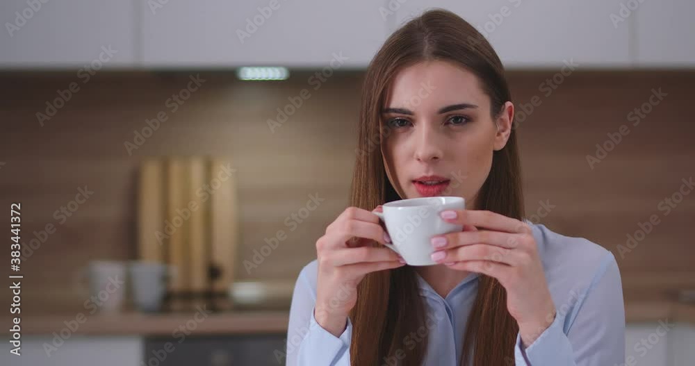 Young female sitting in the kitchen and drinking coffee, looks at the camera, portrait, day off at home. Young female sitting in the kitchen and drinking coffee, looks at the camera, portrait, day off at home.