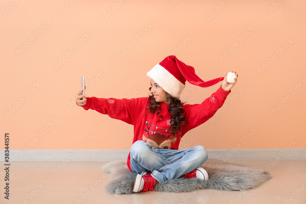 Cute little girl in Santa hat taking selfie near color wall Cute little girl in Santa hat taking selfie near color wall