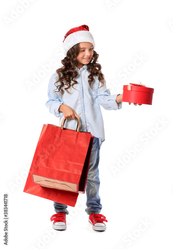 Cute little girl in Santa hat, with shopping bags and gift on white background