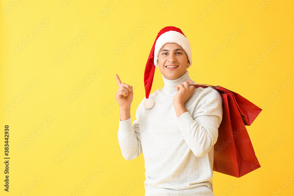 Handsome man in Santa hat and with shopping bags pointing at something on color background Handsome man in Santa hat and with shopping bags pointing at something on color background