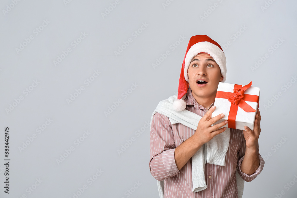 Handsome man in Santa hat and with gift box on grey background Handsome man in Santa hat and with gift box on grey background