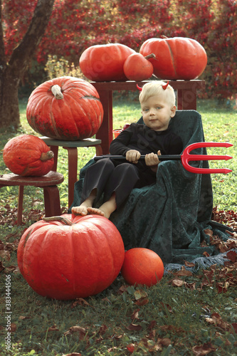 Caucasian child toodler with blue eyes in halloween costume with pumkins. With and devil atributs - devil horns and witch hat 