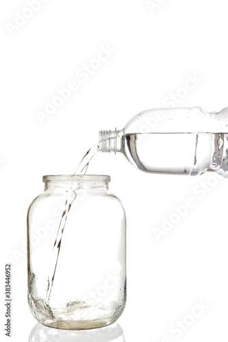 Pouring water into an empty glass jar on a white background