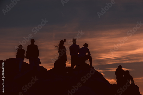 Group of people silhouette admiring a beautiful red and orange sunset in a famous sunset point in Sardinia, Italy. Somebody taking pictures, somebody taking a selfie. Summer feeling.