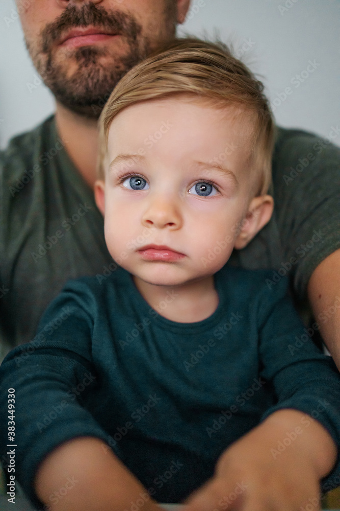 Youngster sitting in father's lap and looking at something with his beautiful big blue eyes. Youngster sitting in father's lap and looking at something with his beautiful big blue eyes.