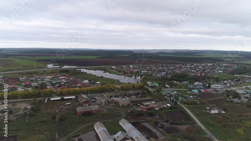 Aerial view of village and farm. There is agricultural machinery on the farm. There is a pond in the village. Cars drive on the roads. Near the village highway, fields and forests. Autumn cloudy day
 photo