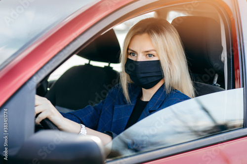 Young girl in black mask sitting in a car, protective mask against coronavirus, driver on a city street during a coronavirus outbreak