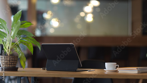 Worktable with digital tablet, coffee cup, notebooks and plant pot in office room