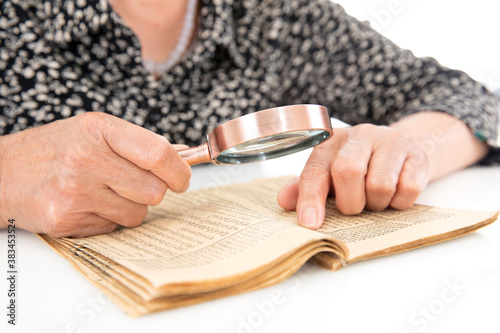 Canvastavla An old man is holding a magnifying glass in hand to look up on an old yellowed b