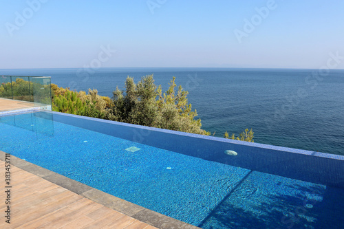 Fototapeta Naklejka Na Ścianę i Meble -  Beach relax and vacation, enjoying life concept. View to the empty swimming pool on sea and trees background