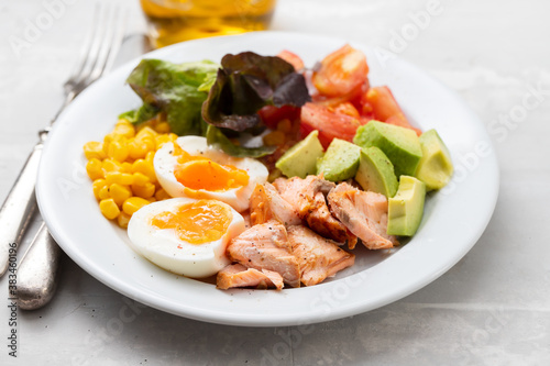 salad salmon with vegetables and boiled egg on white plate on ceramic background