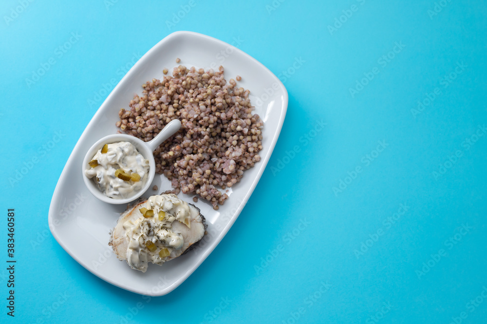 boiled fish with buckwheat and sauce on white dish on blue background boiled fish with buckwheat and sauce on white dish on blue background