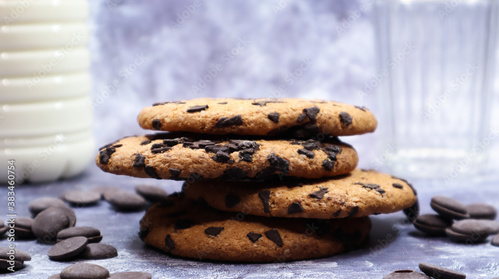 American chocolate chip cookies stacked on top of each other with milk in a glass on a gray background. Traditional rounded crunchy dough with chocolate chips. Bakery. Delicious dessert, pastries. American chocolate chip cookies stacked on top of each other with milk in a glass on a gray background. Traditional rounded crunchy dough with chocolate chips. Bakery. Delicious dessert, pastries.