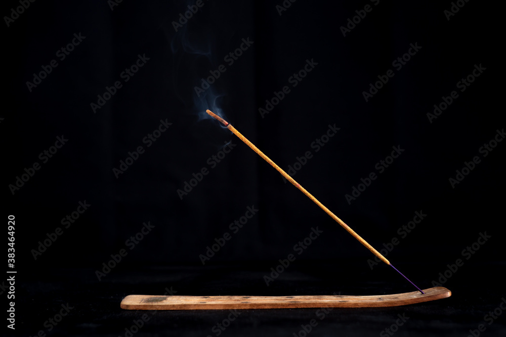 Incense stick with a wisp of smoke on a wooden stand. On a dark background