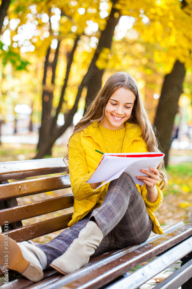 Young girl draws with a pencil in the sketchbook, autumn park outdoor Young girl draws with a pencil in the sketchbook, autumn park outdoor