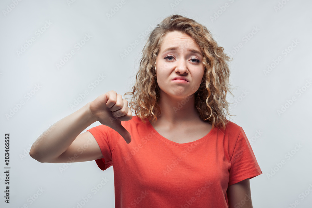 Pretty blonde girl showing thumb down. Unlike, dislike, failure gestures concept. Studio shot, white background Pretty blonde girl showing thumb down. Unlike, dislike, failure gestures concept. Studio shot, white background