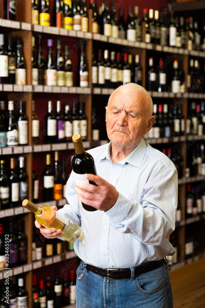 Serious retiree chooses white and red wine in a liquor store. High quality photo