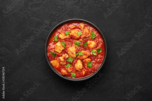 Chicken Madras Curry in black bowl on dark slate table top. Indian cuisine dish with with chicken meat and spicy masala gravy. Asian food and meal. Top view