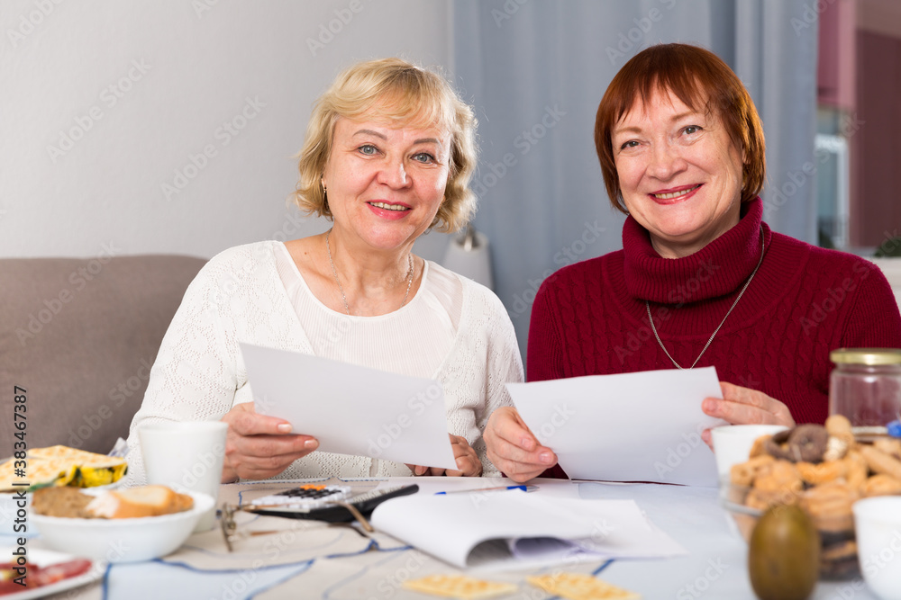 Smiling senior woman explaining some documentation to old female friend at home