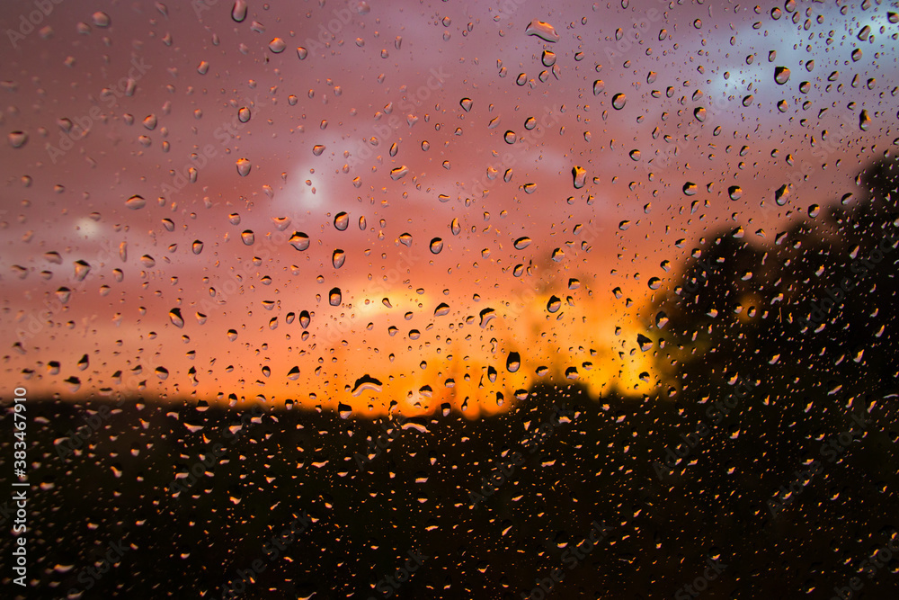 Glass in raindrops view of the sunset forest and storm clouds