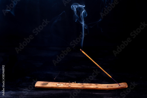 Incense stick with a wisp of smoke on a wooden stand. On a dark background