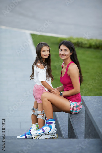 happy little child girl with mother in roller skates in summer park. mom and child are looking at the camera