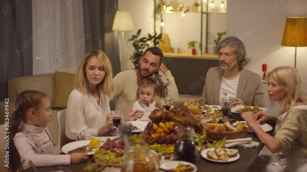 Multi-generation family members sitting together at table talking about something while celebrating Thanksgiving holiday Multi-generation family members sitting together at table talking about something while celebrating Thanksgiving holiday