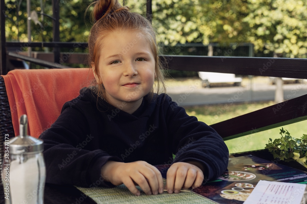 little girl sitting on the summer veranda of a cafe in the park smiling and looking at the camera resting on vacation little girl sitting on the summer veranda of a cafe in the park smiling and looking at the camera resting on vacation
