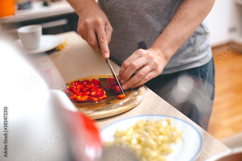 Woman's hands cutting fresh red paprika on chopping board. Cooking at home concept.