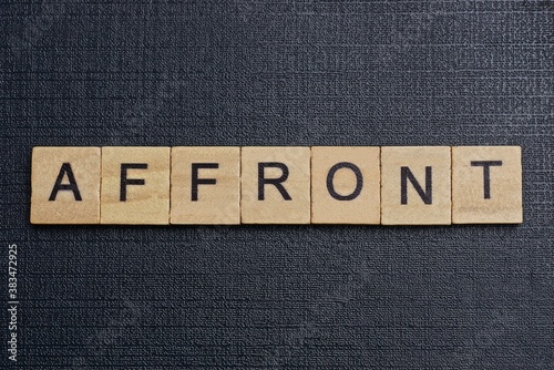 Foto gray word affront from small wooden letters on a black table