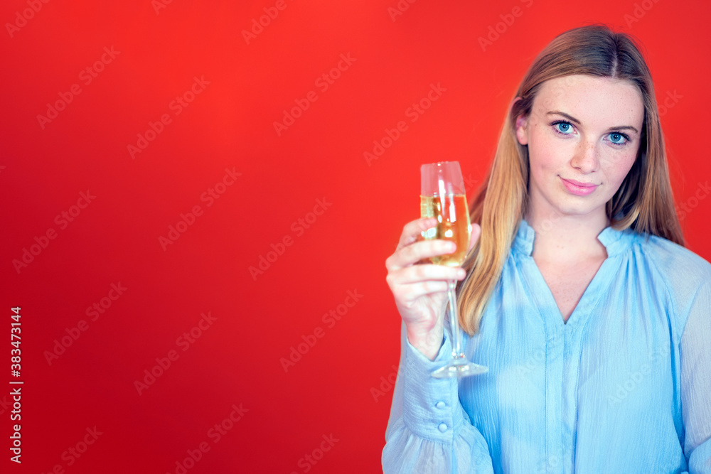 beautiful caucasian young woman with long hair and blue eyes holding a champagne flute and looking to the camera - copy space for advertising in red background beautiful caucasian young woman with long hair and blue eyes holding a champagne flute and looking to the camera - copy space for advertising in red background