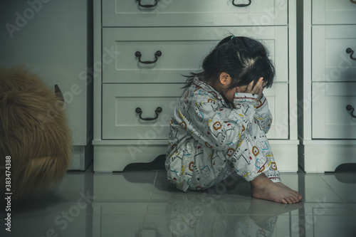 Sad little girl sitting on floor indoors. Child in danger. Sad little girl closing eyes with hands on floor indoors. Child inhuman concept. photo