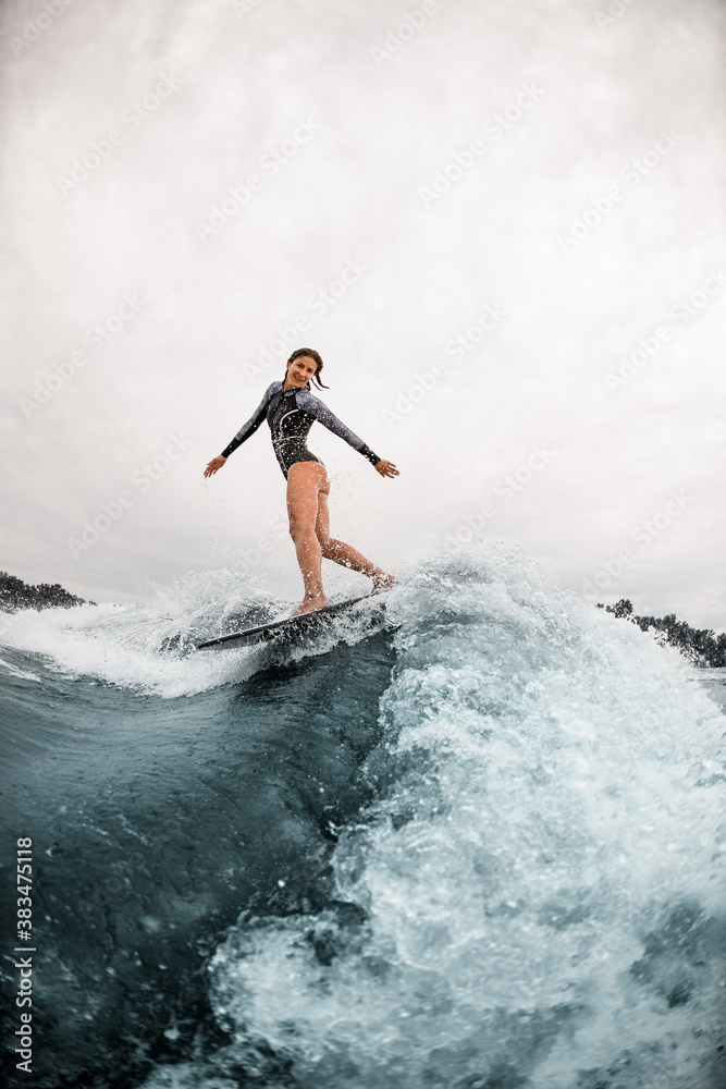 view on pretty smiling woman who elegantly stands on the board and rides down the wave view on pretty smiling woman who elegantly stands on the board and rides down the wave